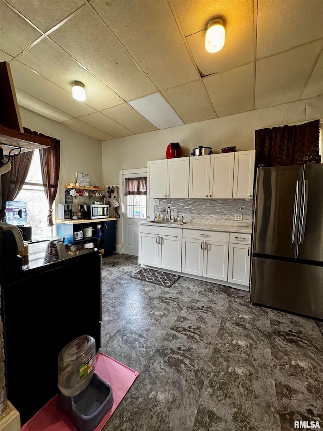 kitchen featuring sink, a drop ceiling, stainless steel appliances, white cabinets, and decorative backsplash