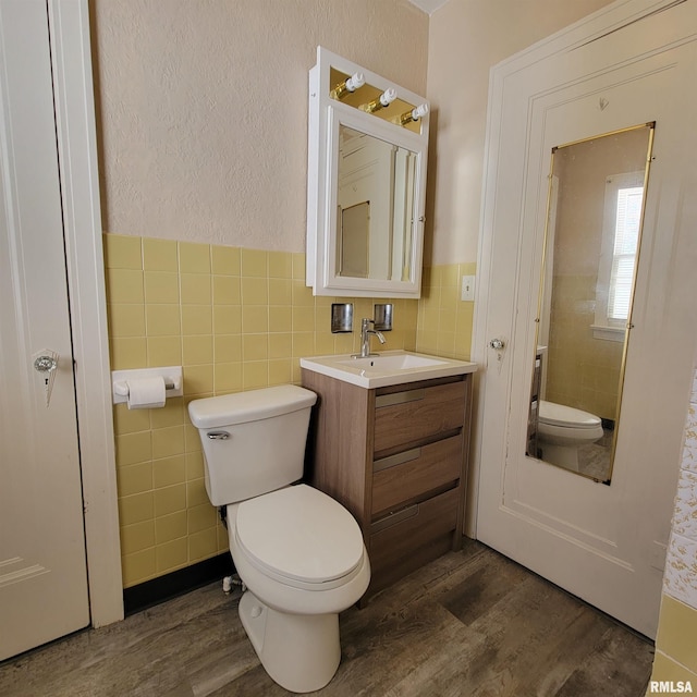 bathroom featuring toilet, vanity, wood-type flooring, and tile walls