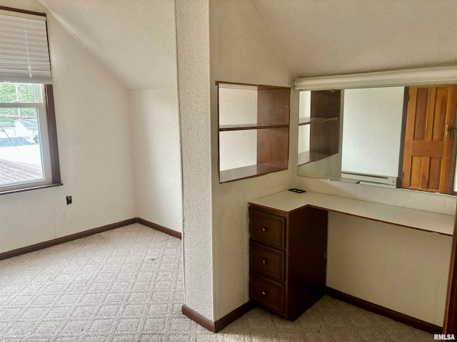 unfurnished office featuring built in desk, light colored carpet, and lofted ceiling