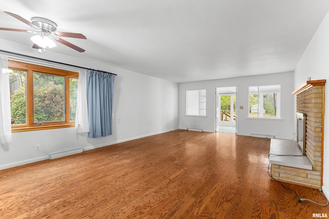 unfurnished living room featuring ceiling fan, wood-type flooring, baseboard heating, and a brick fireplace