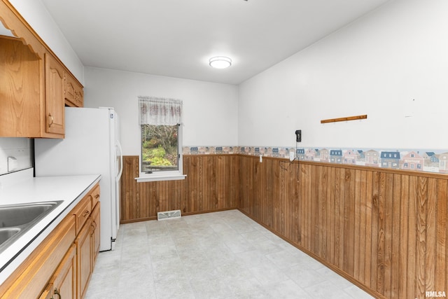 kitchen featuring white fridge, wooden walls, and sink