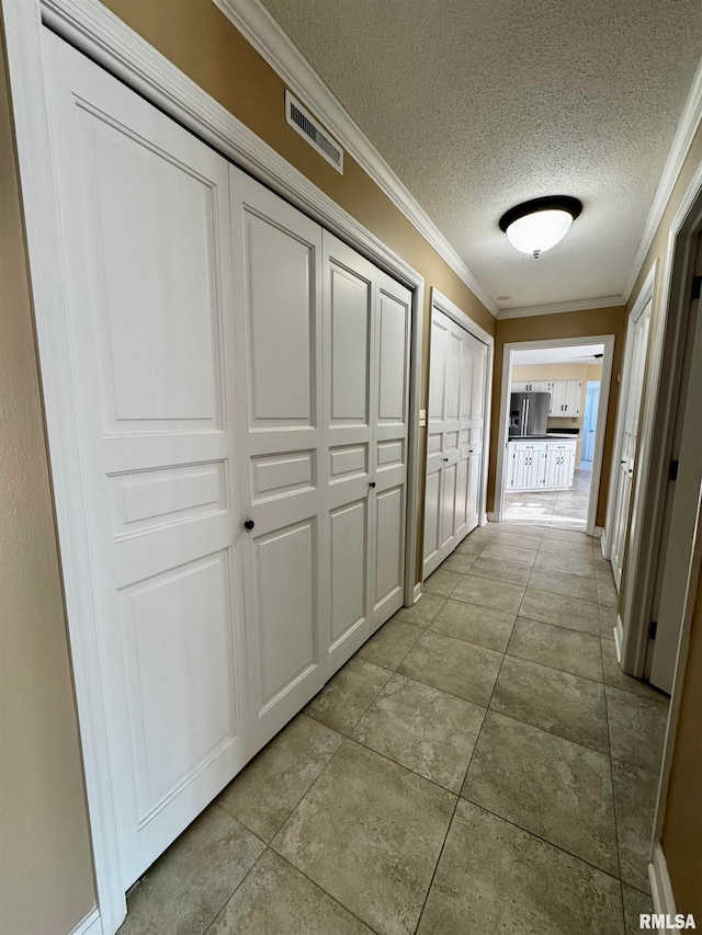 hallway featuring a textured ceiling, light tile patterned floors, and crown molding