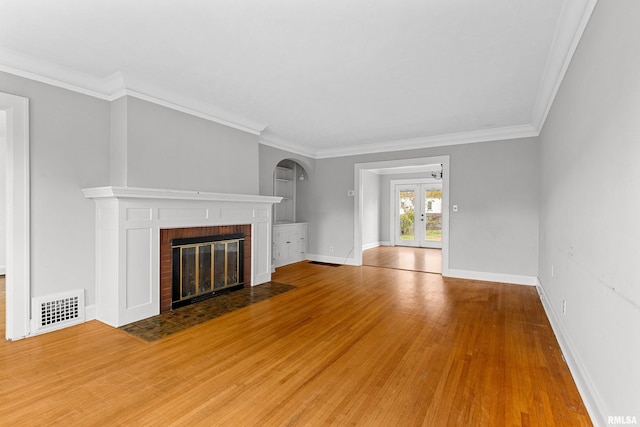 unfurnished living room featuring a fireplace, hardwood / wood-style floors, crown molding, and french doors