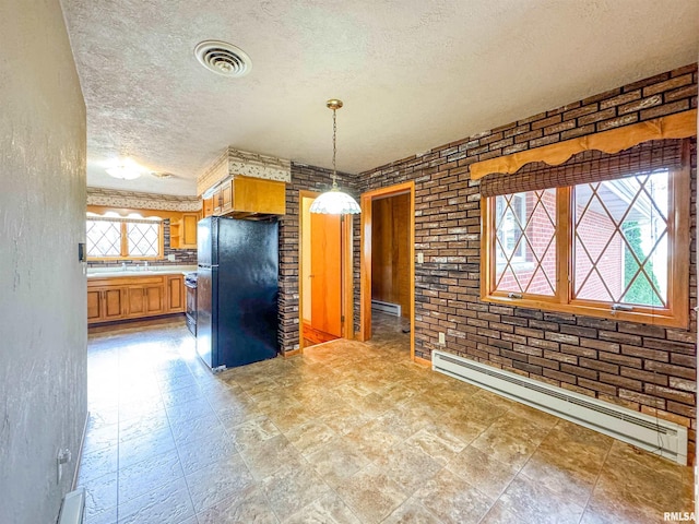 kitchen featuring brick wall, black fridge, baseboard heating, a textured ceiling, and hanging light fixtures