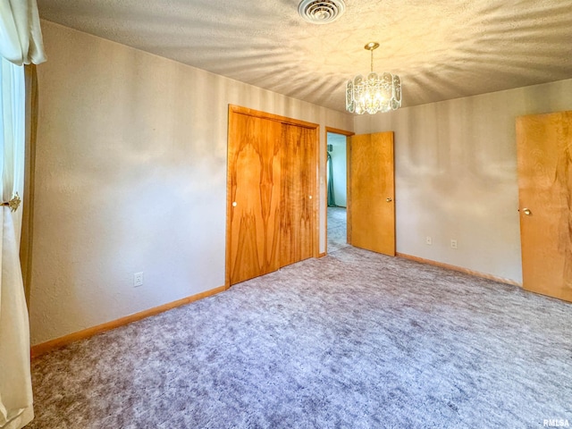 unfurnished bedroom featuring an inviting chandelier, carpet flooring, and a textured ceiling