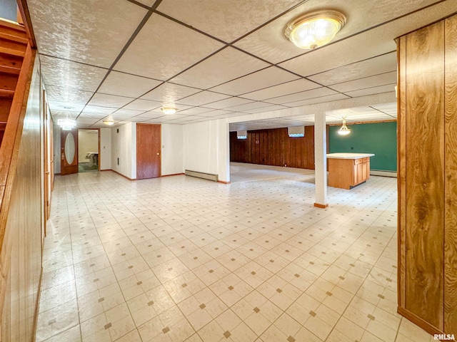 basement featuring a drop ceiling, a baseboard radiator, and wooden walls