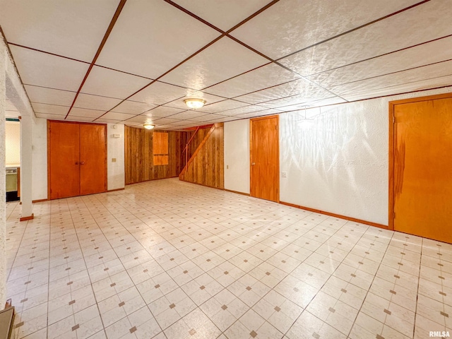 basement featuring a drop ceiling and wood walls