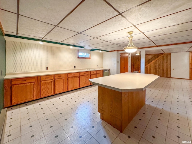 kitchen with wood walls, stainless steel dishwasher, hanging light fixtures, and a center island