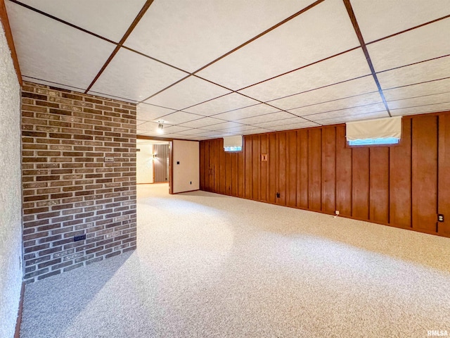 basement featuring a drop ceiling, carpet, and wood walls