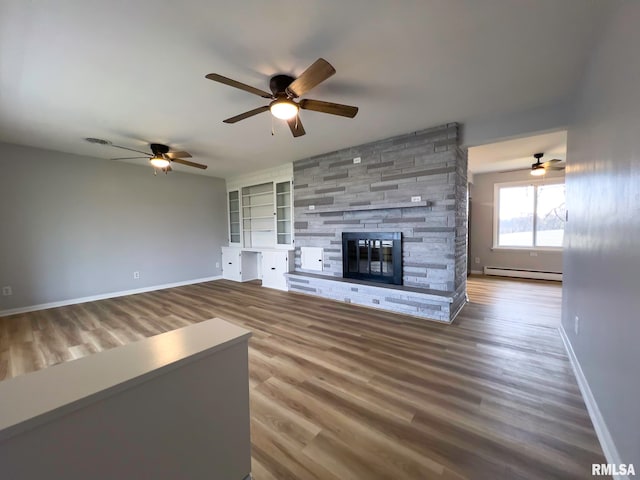 unfurnished living room featuring a stone fireplace, wood-type flooring, baseboard heating, and ceiling fan