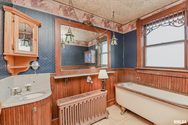 bathroom with vanity, wooden walls, a tub, and radiator