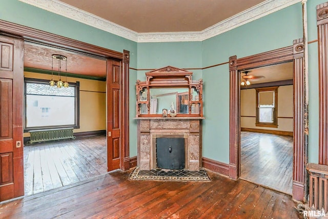 unfurnished living room featuring a tiled fireplace, dark hardwood / wood-style flooring, crown molding, and radiator