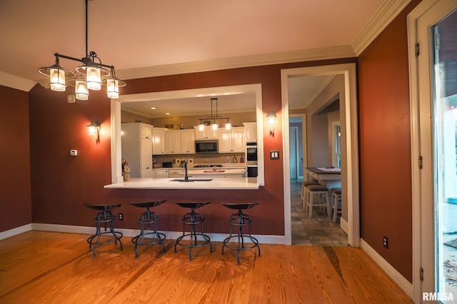 kitchen featuring white cabinets, sink, a breakfast bar area, decorative light fixtures, and stainless steel appliances