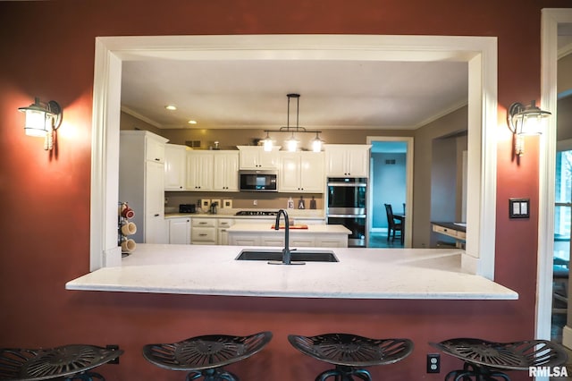 kitchen with sink, crown molding, pendant lighting, white cabinets, and appliances with stainless steel finishes