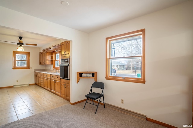 kitchen with light tile patterned floors, sink, black oven, ceiling fan, and a baseboard heating unit