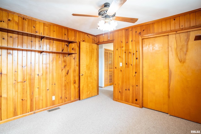 unfurnished bedroom with ceiling fan, ornamental molding, light carpet, a closet, and wood walls