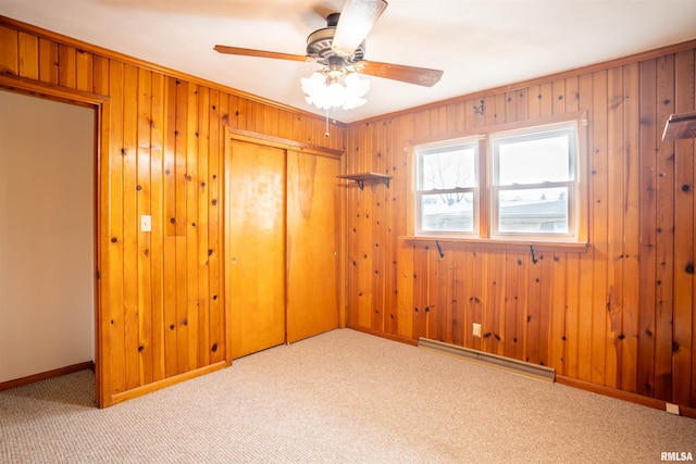 unfurnished bedroom with light carpet, baseboard heating, ornamental molding, wooden walls, and a closet