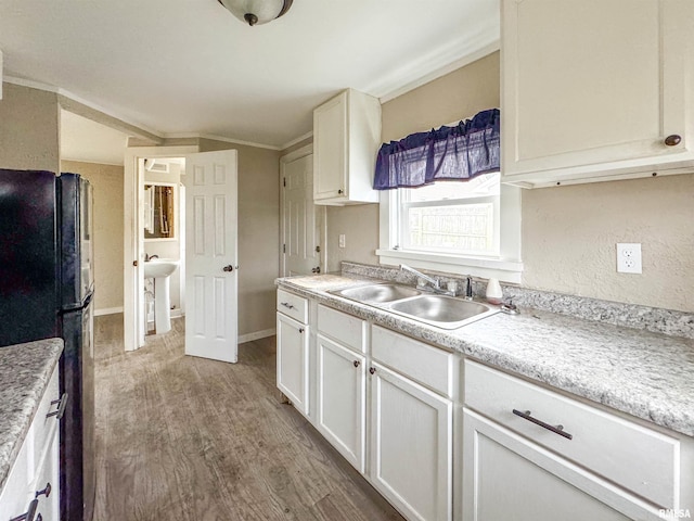 kitchen featuring black refrigerator, white cabinetry, light hardwood / wood-style flooring, and sink