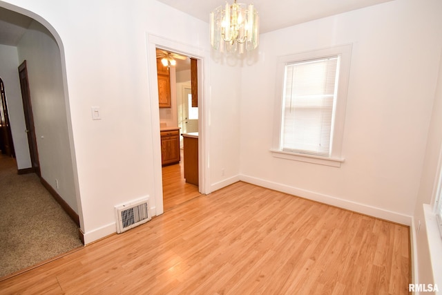 spare room with light hardwood / wood-style flooring and a notable chandelier