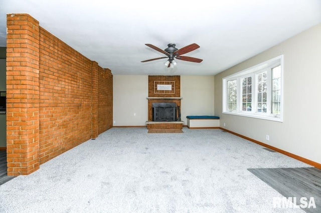 unfurnished living room featuring ceiling fan, brick wall, carpet floors, and a fireplace