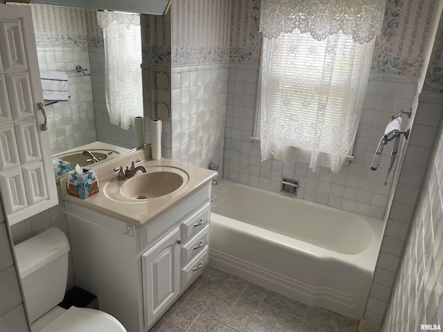 bathroom with a tub, tile patterned flooring, toilet, vanity, and tile walls