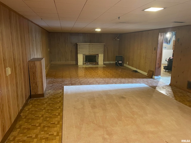 basement featuring wood walls, light parquet floors, and a brick fireplace