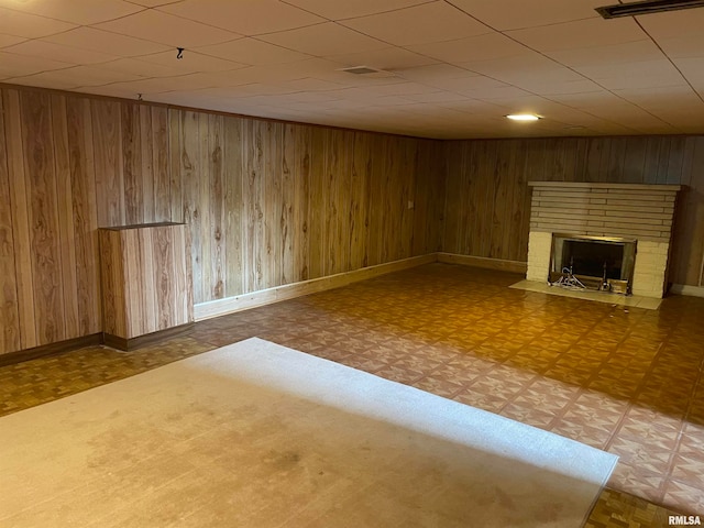 basement featuring parquet flooring, wooden walls, and a brick fireplace