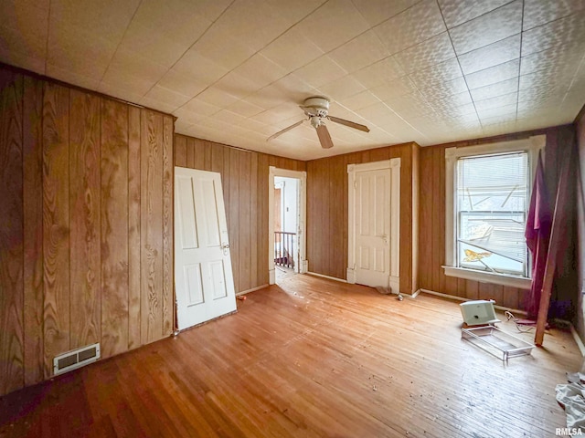 unfurnished bedroom with light hardwood / wood-style flooring, ceiling fan, and wooden walls