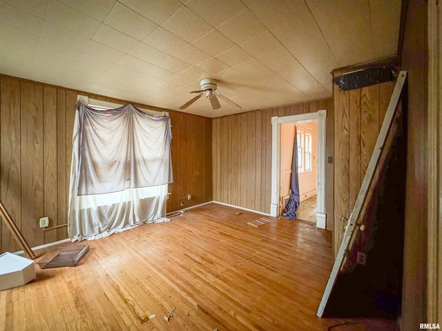 unfurnished room featuring hardwood / wood-style floors, ceiling fan, and wooden walls