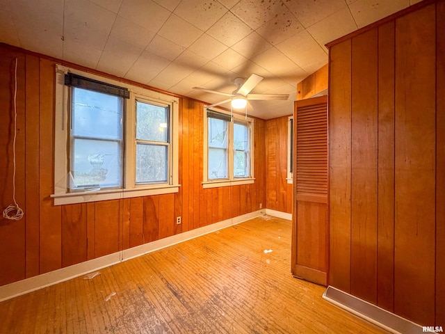 empty room featuring wood walls, ceiling fan, and light hardwood / wood-style floors