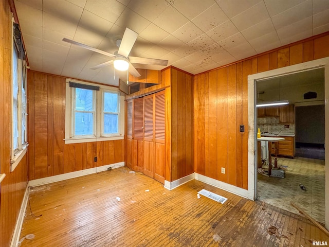 unfurnished bedroom featuring wooden walls, ceiling fan, and hardwood / wood-style flooring