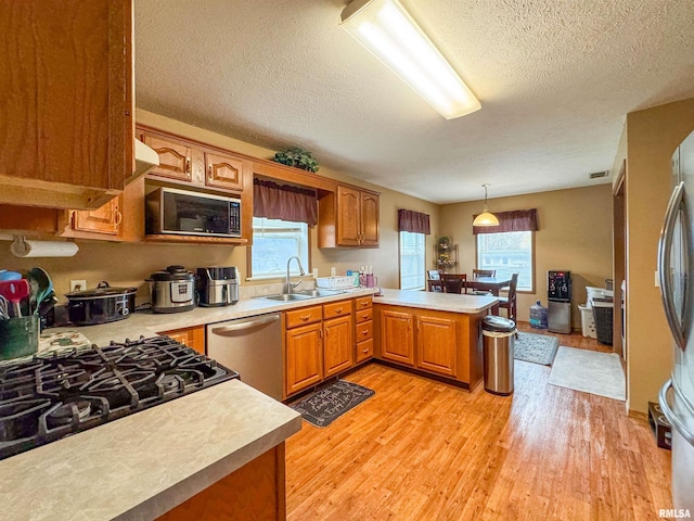 kitchen with sink, hanging light fixtures, light wood-type flooring, appliances with stainless steel finishes, and kitchen peninsula