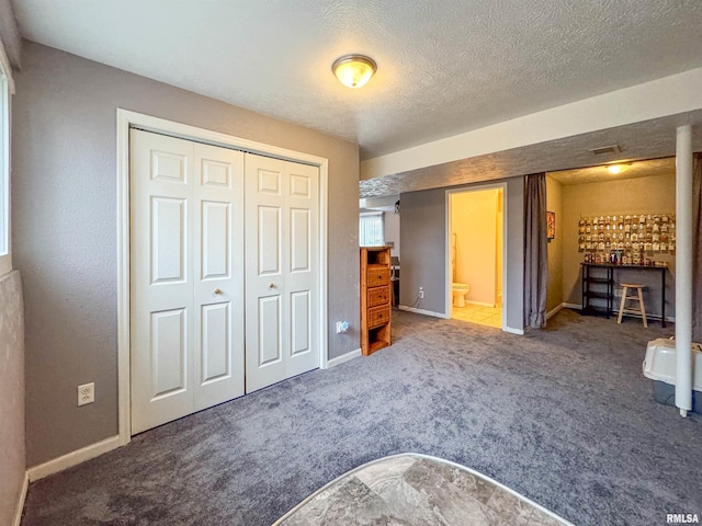 unfurnished bedroom with carpet flooring, ensuite bath, a closet, and a textured ceiling