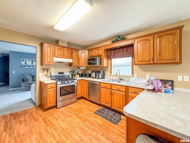 kitchen featuring sink, stainless steel appliances, kitchen peninsula, a textured ceiling, and light wood-type flooring