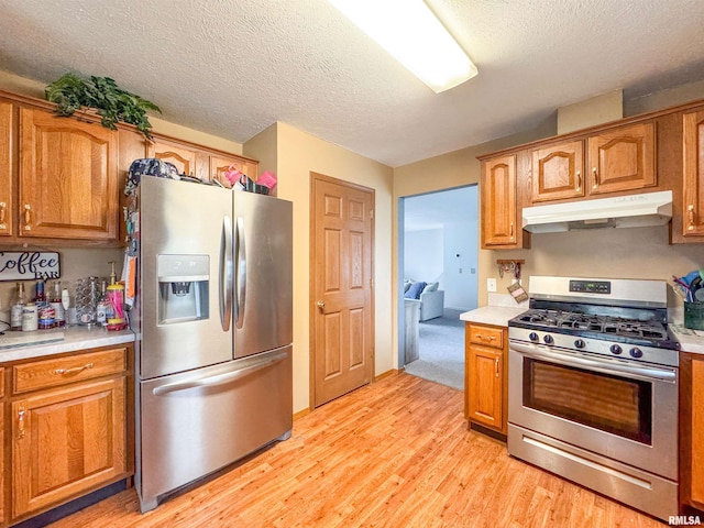 kitchen with a textured ceiling, stainless steel appliances, and light hardwood / wood-style flooring