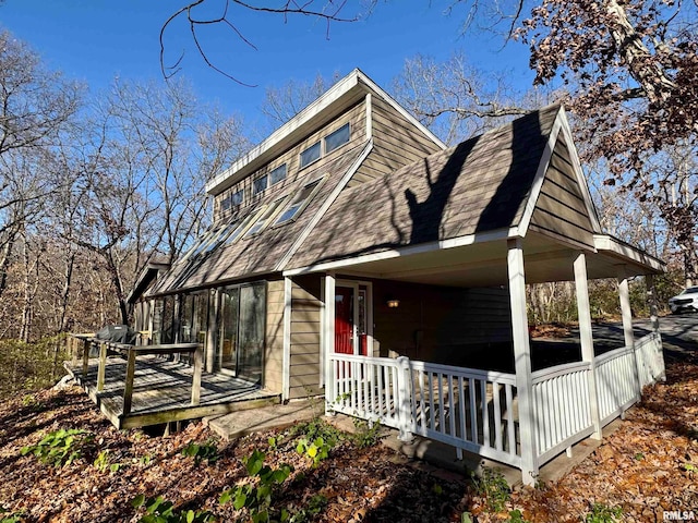 view of side of home with covered porch and a shingled roof