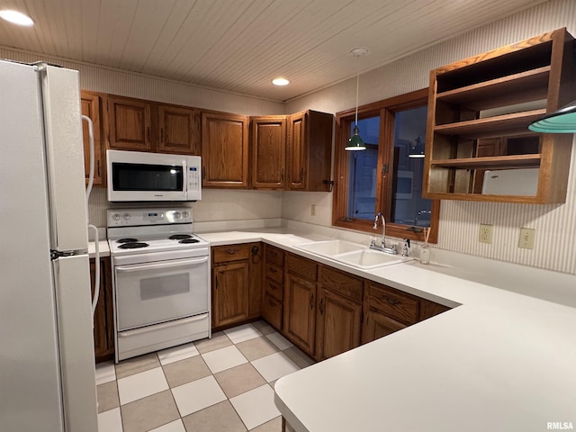 kitchen featuring pendant lighting, light countertops, brown cabinetry, a sink, and white appliances