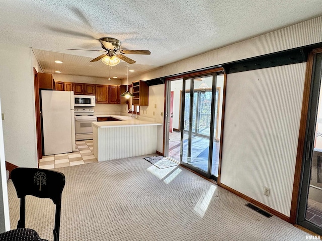 kitchen featuring a peninsula, white appliances, visible vents, light countertops, and brown cabinetry