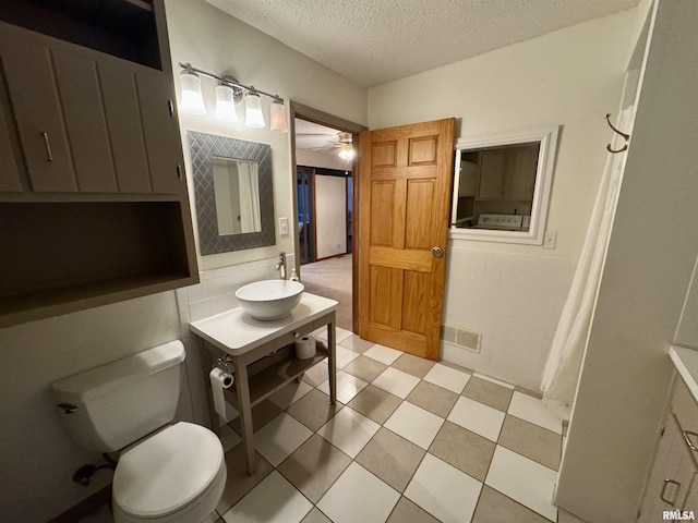 bathroom with a textured ceiling, toilet, a sink, visible vents, and tile walls