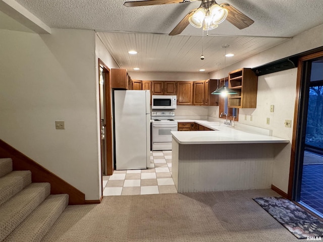 kitchen featuring light countertops, brown cabinetry, a sink, white appliances, and a peninsula