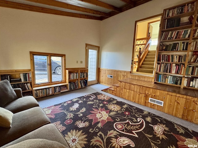 living area with carpet floors, a wainscoted wall, visible vents, beamed ceiling, and stairs