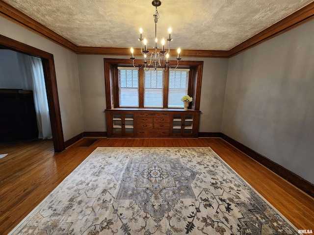 unfurnished dining area featuring a textured ceiling, crown molding, a chandelier, and dark hardwood / wood-style floors