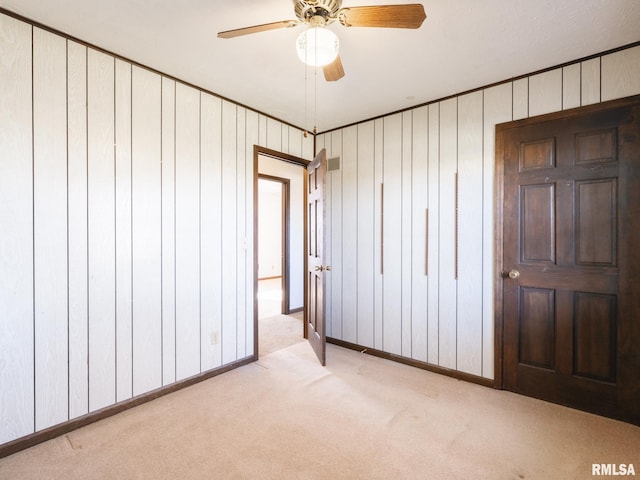 unfurnished bedroom with light carpet, ceiling fan, and wooden walls