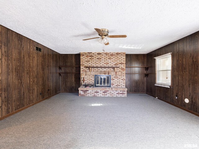 unfurnished living room with a textured ceiling, a fireplace, wood walls, and light carpet