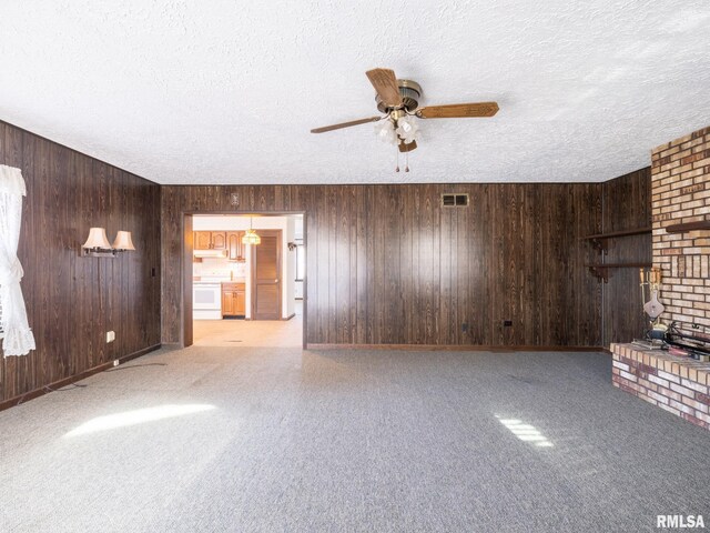 unfurnished living room featuring ceiling fan, wood walls, and a textured ceiling