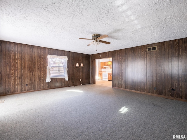 carpeted empty room with a textured ceiling, ceiling fan, and wood walls