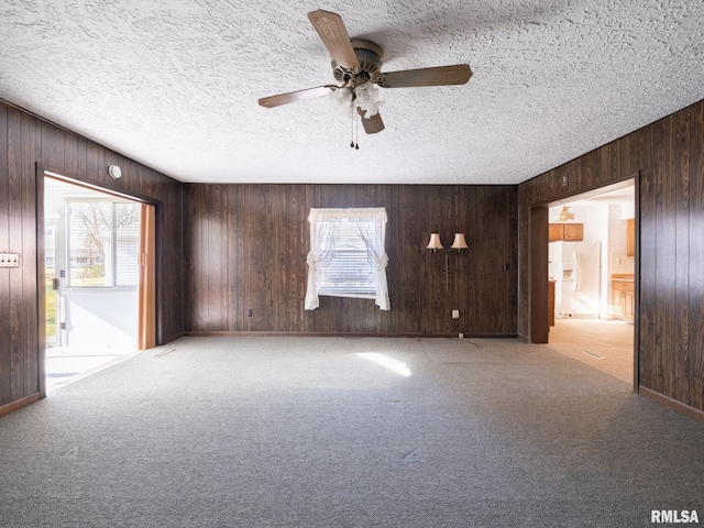 carpeted empty room with a textured ceiling, ceiling fan, and wood walls