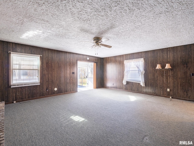 carpeted empty room with wood walls, plenty of natural light, and ceiling fan