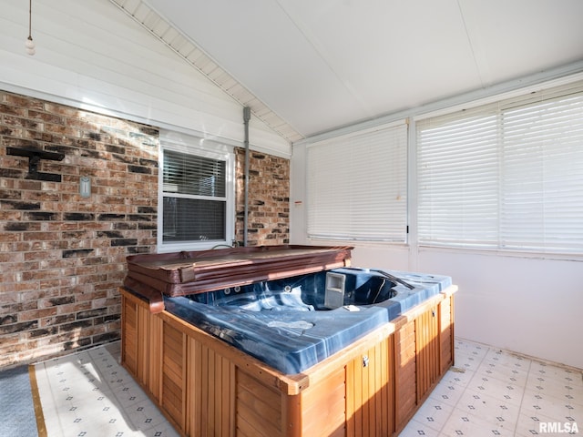 interior space with lofted ceiling, brick wall, and a hot tub