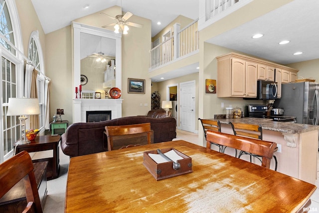 dining area featuring a tile fireplace, ceiling fan, and high vaulted ceiling